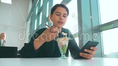 机场等待飞机航班.. 十几岁的女孩吃沙拉的生活方式，看起来像智能手机。 在咖啡馆里上网。 机场